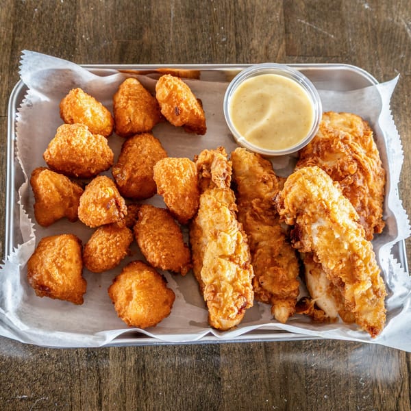 Fried chicken tenders and golden-brown tater tots with a side of dipping sauce on a metal tray.