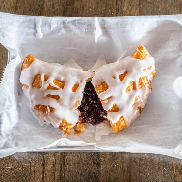 A southern fried pie, split open to reveal dark berry filling, covered in white icing.