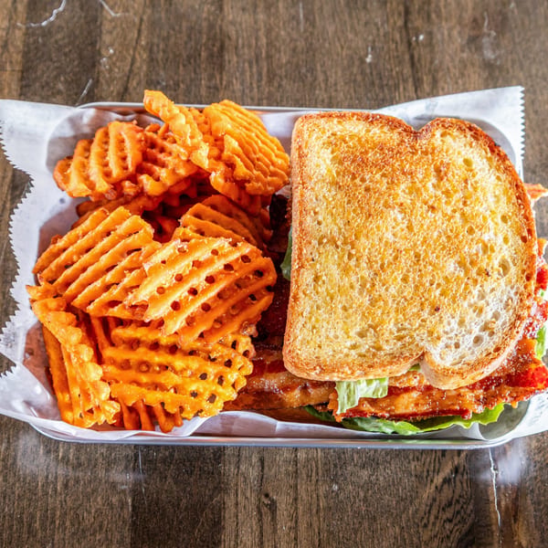 Southern BLT sandwich with crispy bacon, lettuce, and tomato, served with a side of waffle fries.
