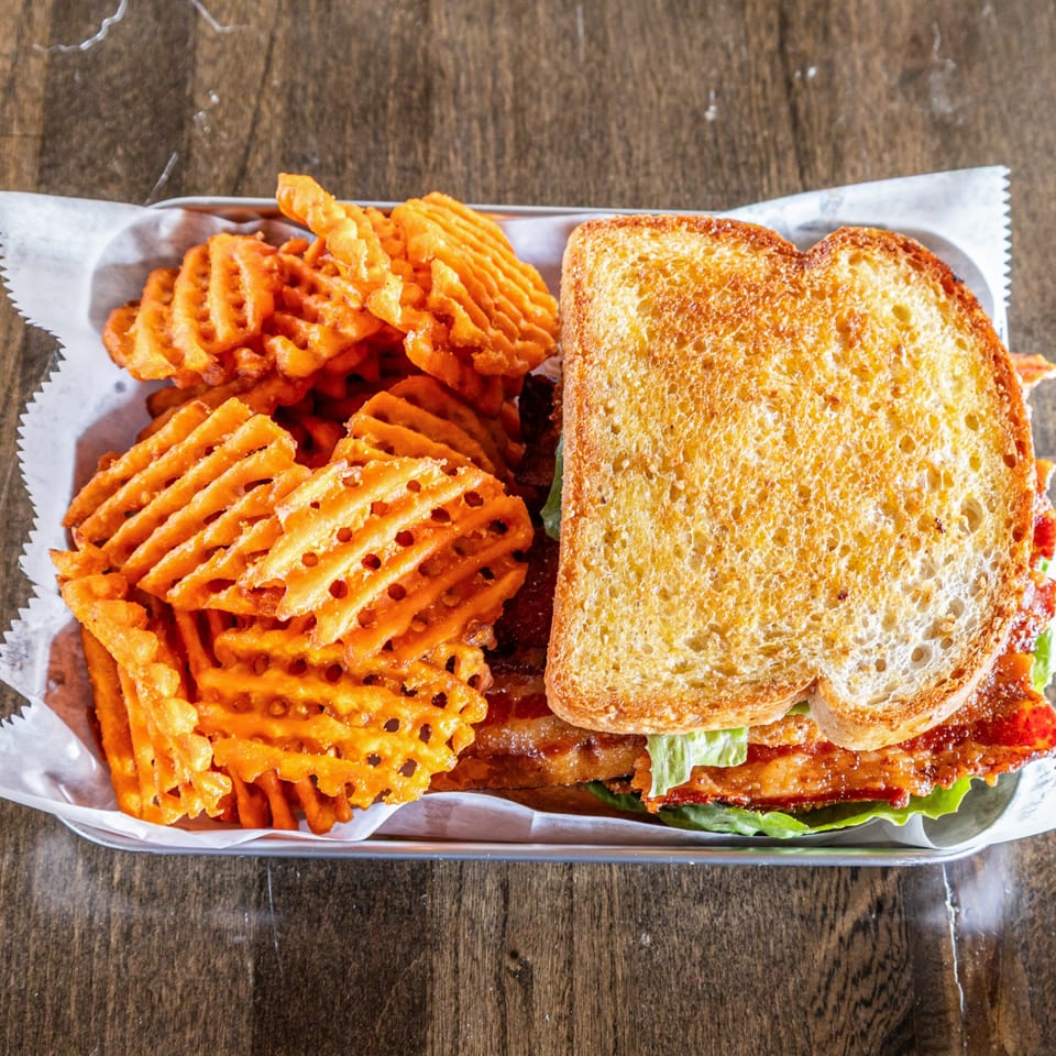 Southern BLT sandwich with crispy bacon, lettuce, and tomato, served with a side of waffle fries.