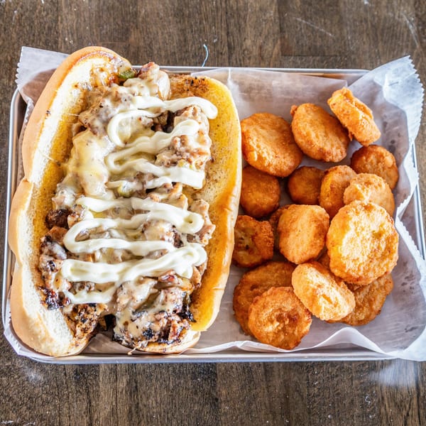 Cheesesteak sandwich with melted cheese and mayonnaise, served with a side of crispy tater tots.