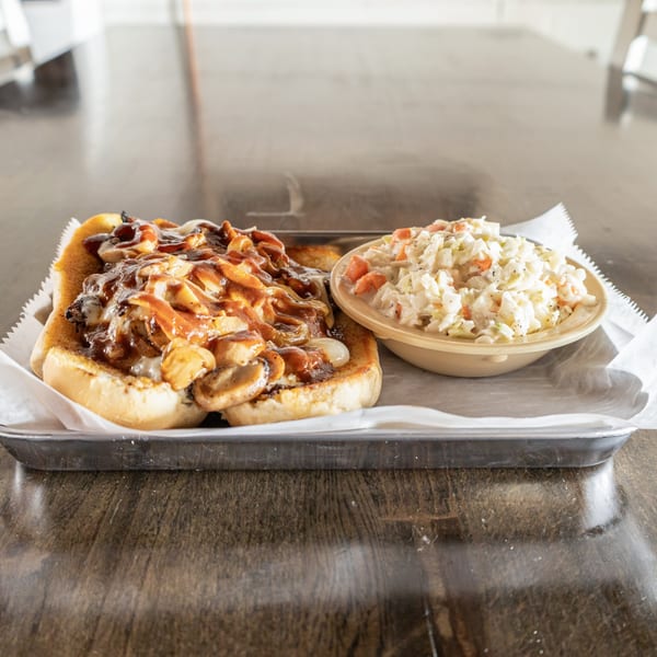 A southern BBQ sandwich with mushrooms and onions, served with a side of coleslaw on a metal tray.