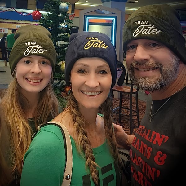 Three smiling people wearing "Team Tater" beanies pose in front of a decorated Christmas tree.